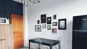 Eine moderne Küche mit einem schwarzen Kühlschrank, einem Holzkabinett und einem Esstisch mit klaren Stühlen. An der Wand befinden sich mehrere gerahmte Bilder.