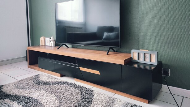 Ein modernes Wohnzimmer mit einem Flachbildfernseher auf einem Holzboden, einer schwarzen Unterhaltungsanlage und einer grünen, strukturierten Wand.