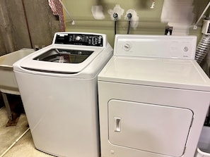 Ein Waschbereich mit zwei weißen Waschmaschinen, einem Waschbecken und einer Wand mit freiliegenden Rohren.