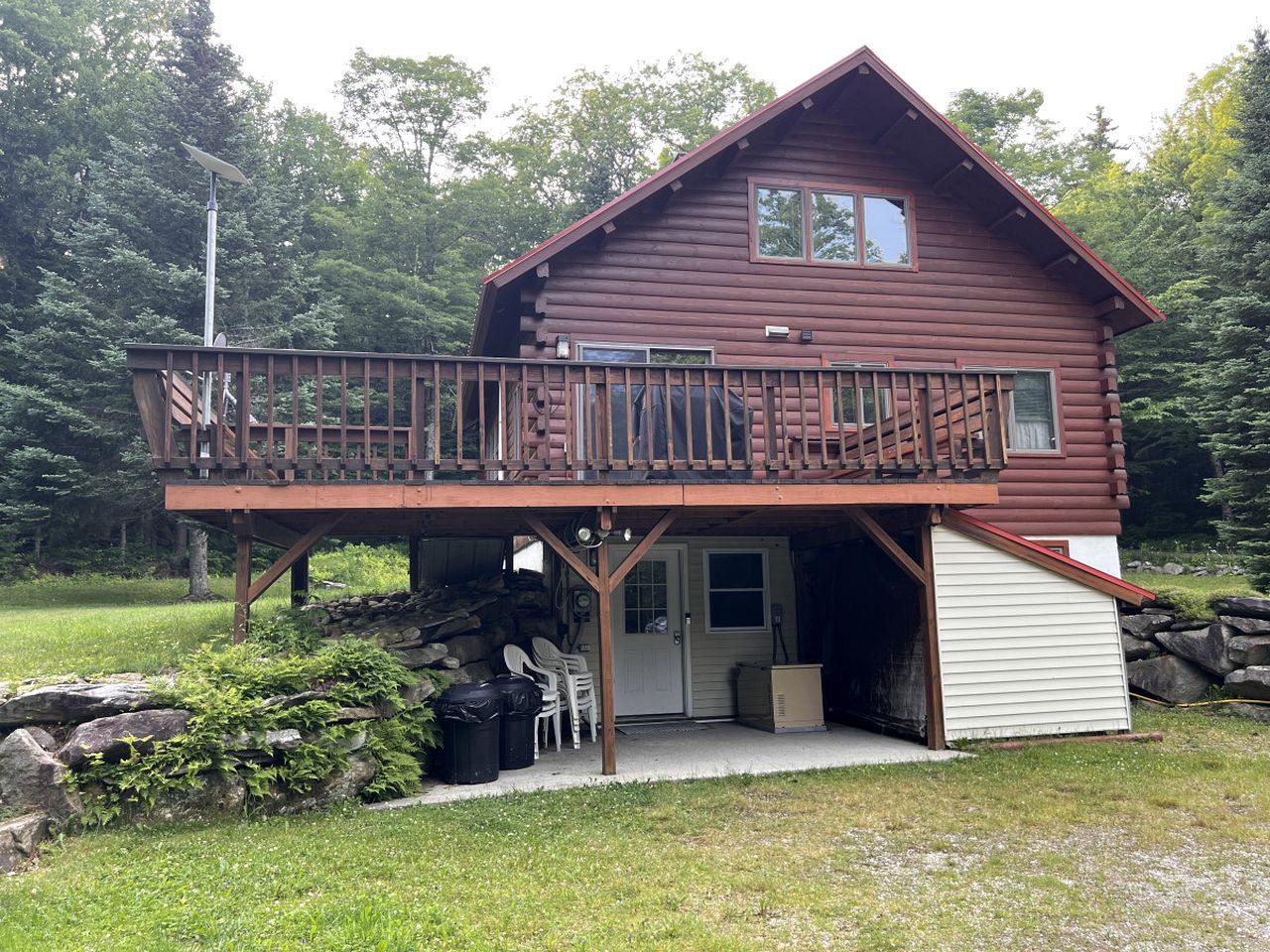 Une cabane en rondins à deux étages, dotée d’un balcon, d’un garage et d’un mur de pierres en arrière-plan.
