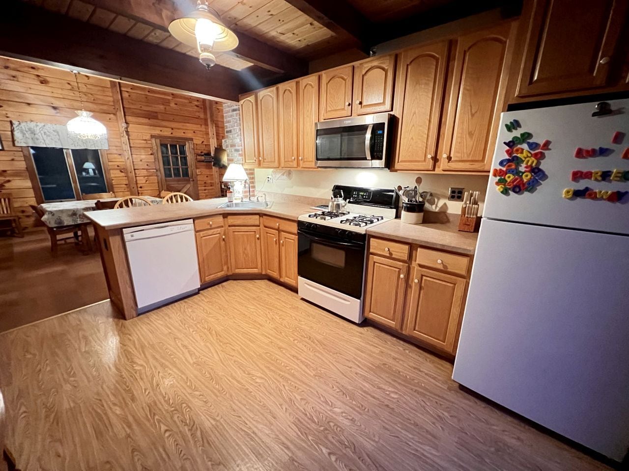 Una cocina con gabinetes de madera, un microondas, una estufa y un refrigerador.