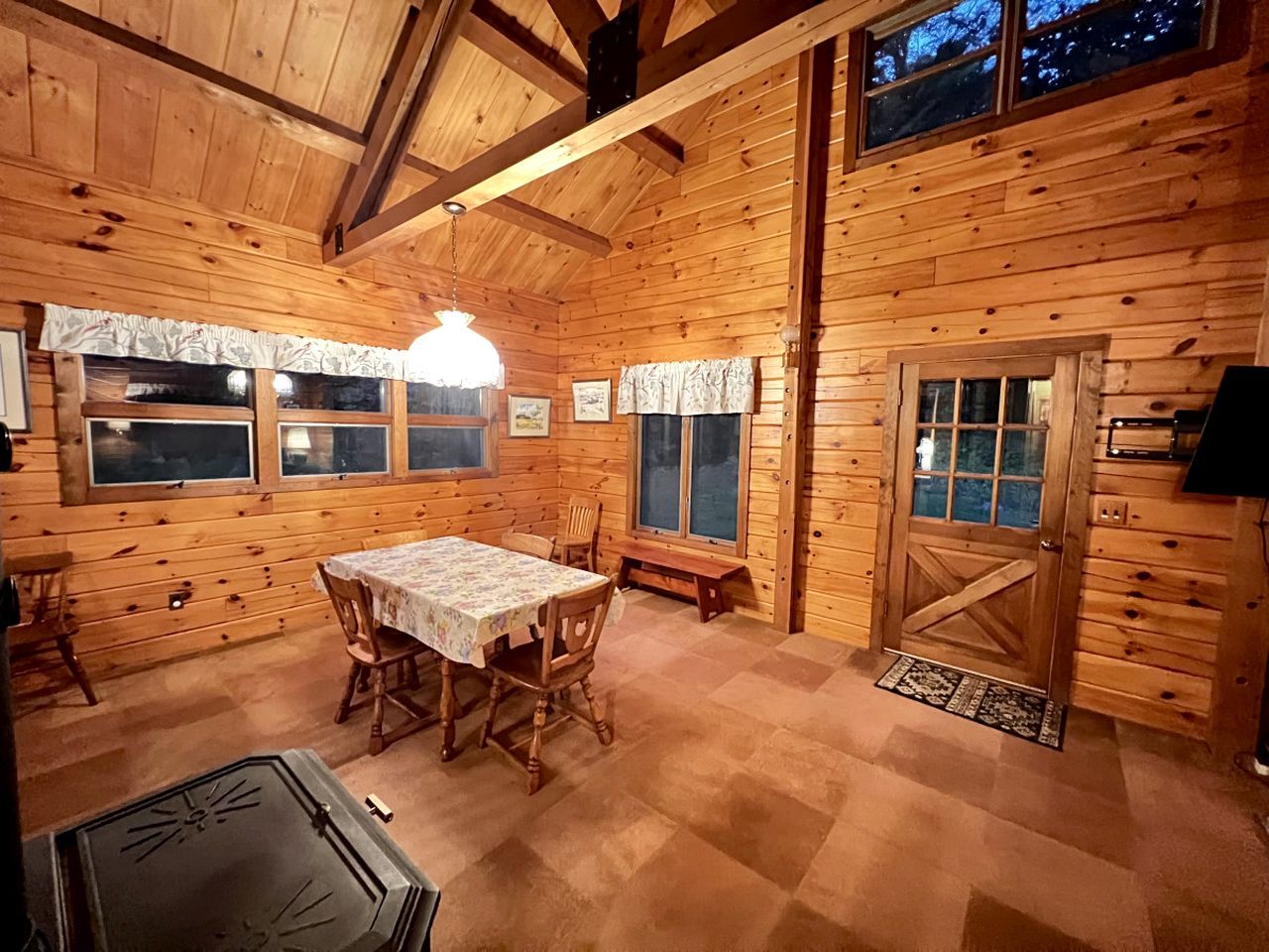Interior de una cabaña de madera con una mesa de comedor, sillas, un banco y una puerta.
