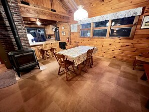 L’intérieur d’un chalet en bois, avec une table à manger, des chaises, une cheminée et une fenêtre donnant sur un paysage enneigé.