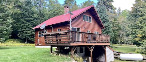 A wooden cabin with a red roof, a deck, and a garage.