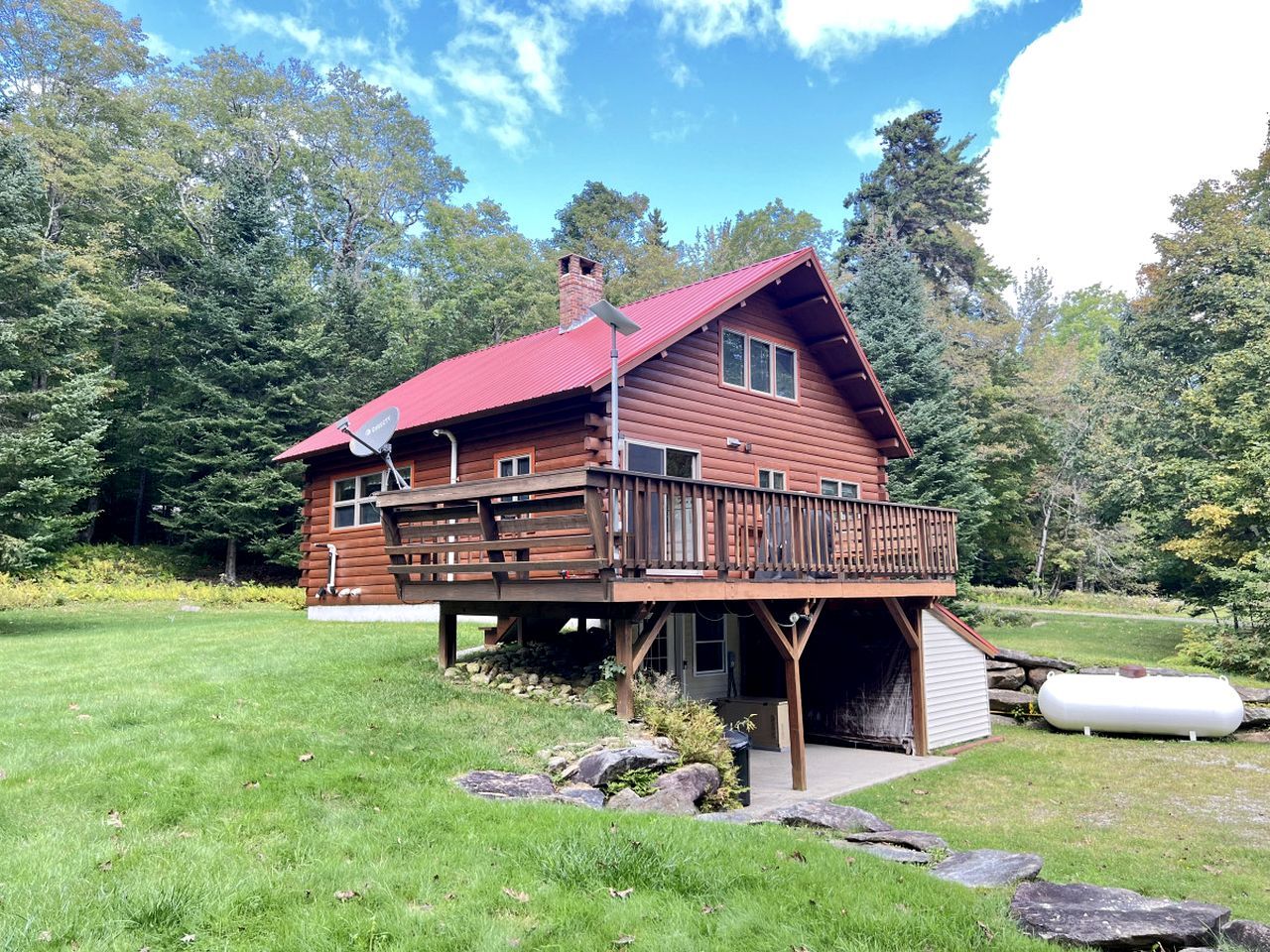 A wooden cabin with a red roof, a deck, and a garage.