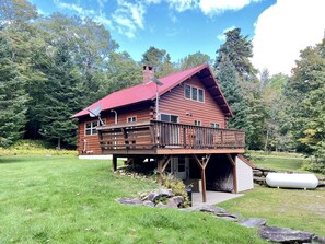 Une cabane en bois avec un toit rouge, une terrasse et un garage.