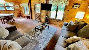 Ein Holzblockhaus-Interieur mit einer Couch, einem Couchtisch, einem Fernseher und einer Essecke.
