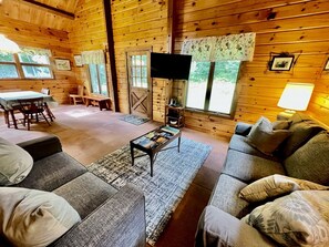 A wooden cabin interior with a sofa, a coffee table, a TV, and a dining area. - Fantastic Lakefront Wooden Cabin Settled Between Trees in Stratton, Vermont (Stratton)