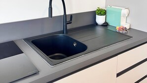 Eine moderne Küche mit einem eleganten schwarzen Spülbecken, einem kleinen Topfpflanzen und einer Kaffeemaschine auf der Arbeitsplatte.