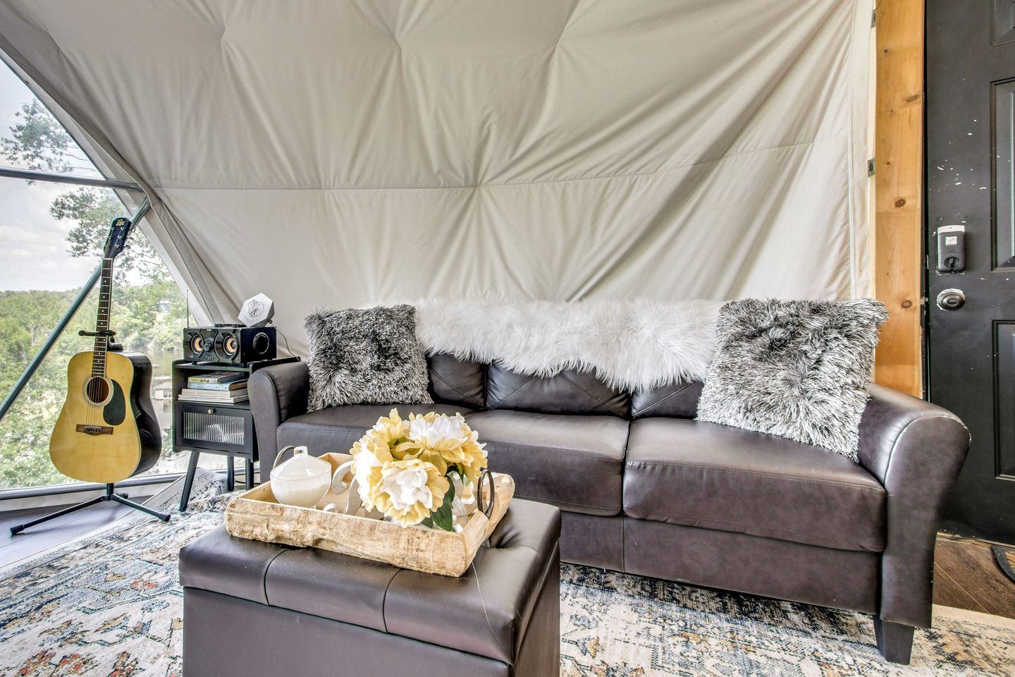 A tented room with a leather sofa, a guitar, and a tray with flowers.
