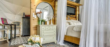 Ein gemütliches Schlafzimmer mit Bett, Kommode, Spiegel und einem Fenster mit Vorhängen.