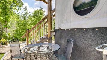 Een terras met metalen stoelen en een tafel, een houten trap en een gebouw met een rond raam.