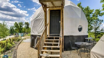 A geodesic dome structure with a wooden staircase leading to a door, surrounded by outdoor seating and vegetation.