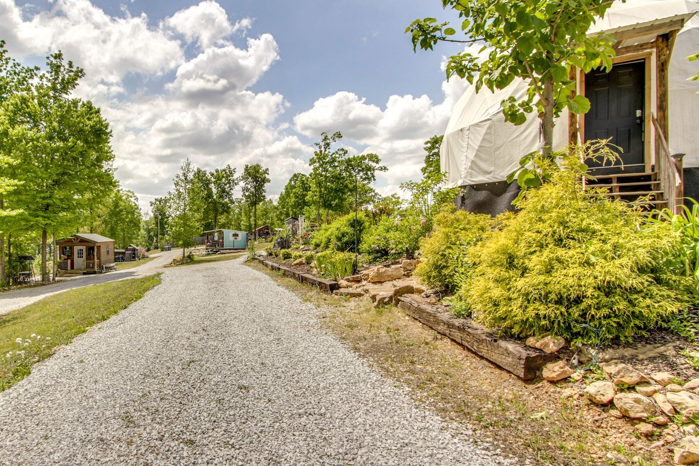 A gravel driveway leading to a building with a covered porch, surrounded by greenery and trees.