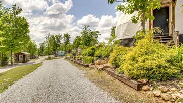 A gravel driveway leading to a building with a covered porch, surrounded by greenery and trees.