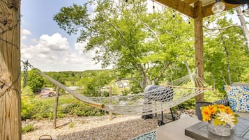 A hammock under a wooden pergola with a view of a green landscape and a house in the background.