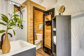 A compact bathroom with a wooden vanity, a white sink, and a toilet. - Riverfront Dome with Outdoor Living and Sunset Views in Alabama (Rogersville)