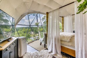 A bedroom with a large window, a bed, a bedside table, and a wardrobe. - Riverfront Dome with Outdoor Living and Sunset Views in Alabama (Rogersville)