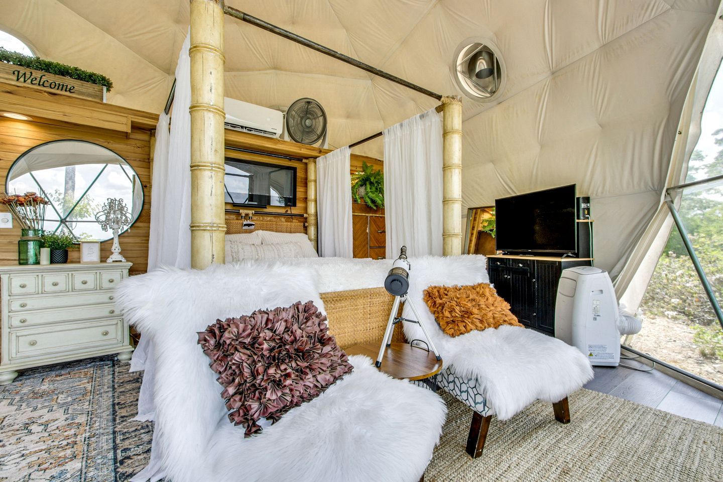 A tented room with a bed, a television, a fan, and a view of the outdoors.