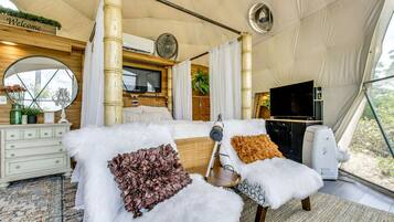A tented room with a bed, a television, a fan, and a view of the outdoors.