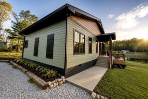 Uma casa moderna térrea, com varanda coberta e um pequeno deck, cercada por um gramado bem cuidado e uma entrada de automóveis com cascalho.