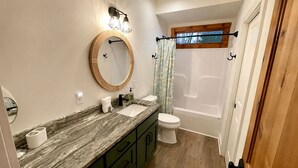 Un baño con encimera de mármol, un espejo redondo, un inodoro y una bañera.