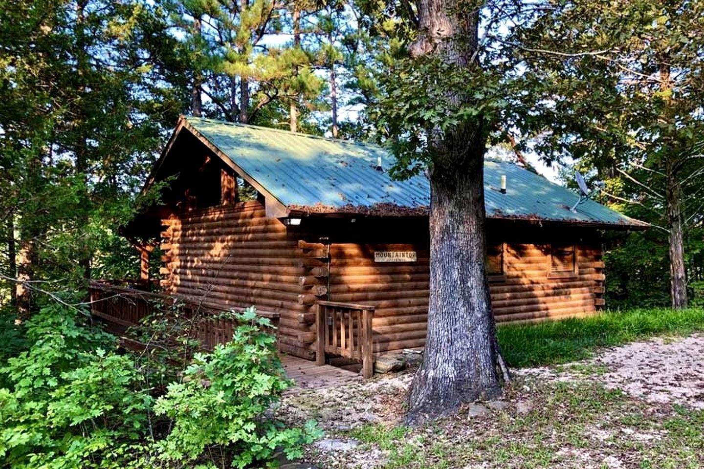 Eine rustikale Holzhütte mit Metalldach, umgeben von Bäumen und einer Holzterrasse.