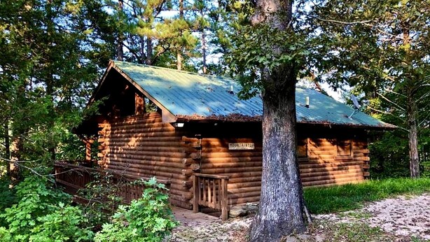 A rustic log cabin with a metal roof, surrounded by trees and a wooden deck. - Rustic Cabin with Indoor Bath Spa and Deck in Arkansas (Eureka Springs)