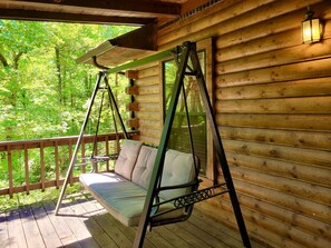 Una cabaña de madera con una mecedora en el porche, con vista a un bosque.