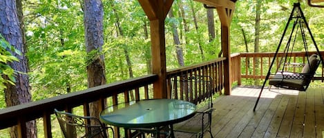 Une terrasse en bois avec une table et des chaises, entourée d’arbres.