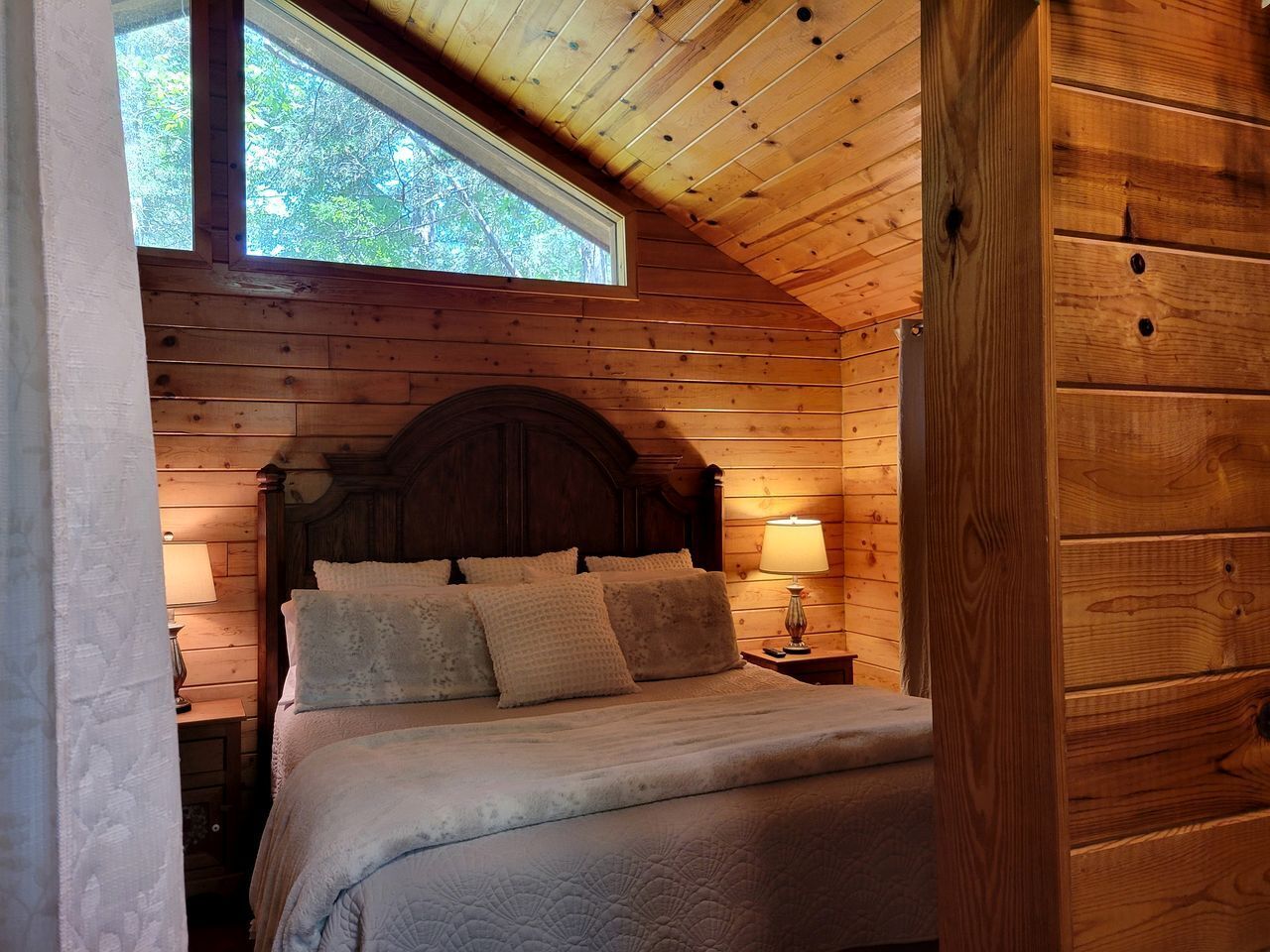 Une chambre dans une cabane en bois, avec un lit, des oreillers, une table de chevet et une fenêtre.