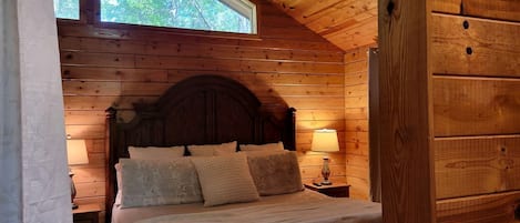 Une chambre dans une cabane en bois, avec un lit, des oreillers, une table de chevet et une fenêtre.