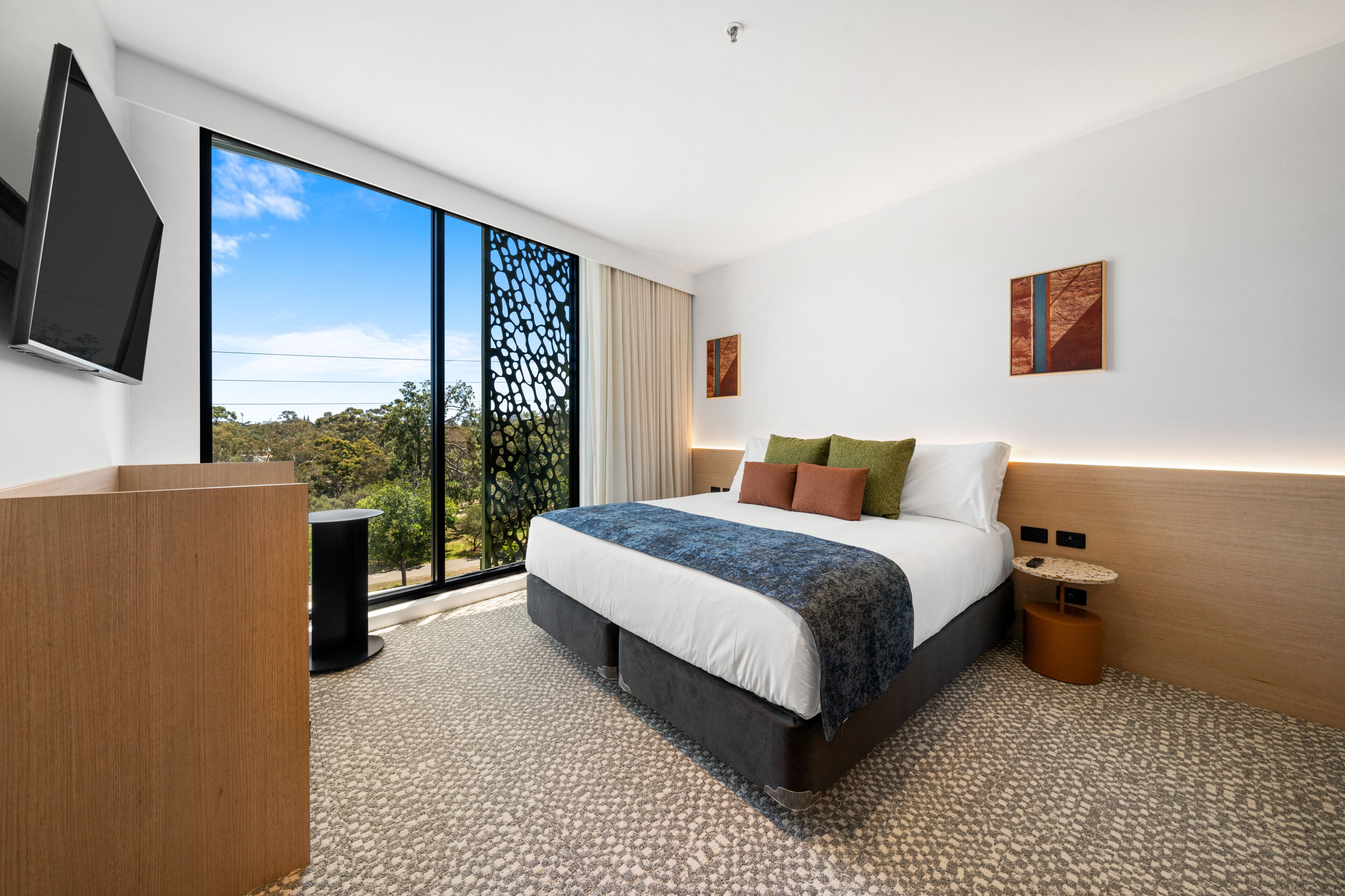 Una habitación de hotel moderna con una cama grande, un televisor de pantalla plana, un escritorio y vistas al exterior.