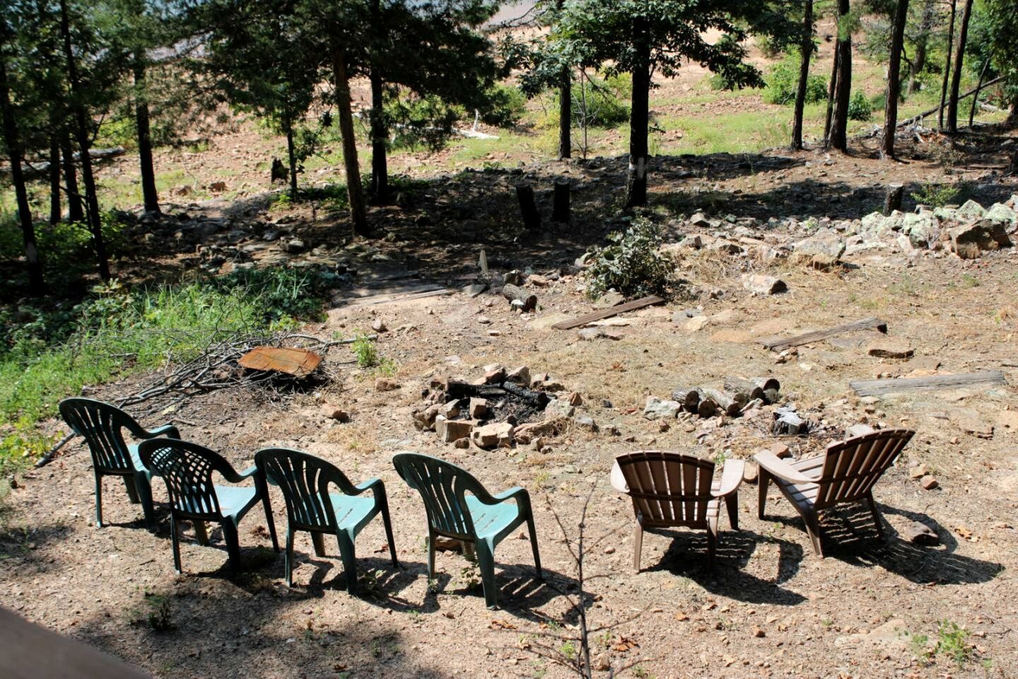 An outdoor seating area with chairs and a table, surrounded by trees and a rocky ground.