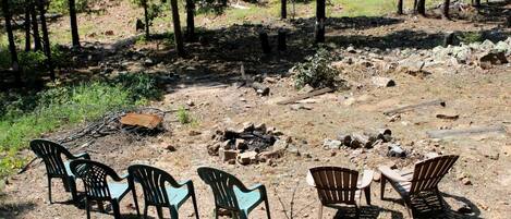 An outdoor seating area with chairs and a table, surrounded by trees and a rocky ground.