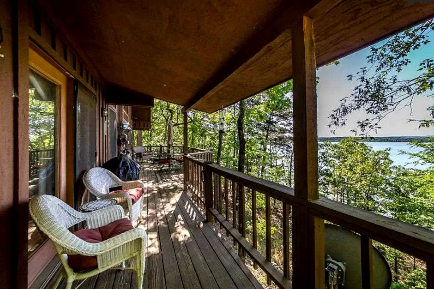 A wooden deck with wicker chairs and a table, overlooking a lake and forest.