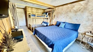 A bedroom with a large bed, bunk beds, a desk with a laptop, and a small table with a lamp.