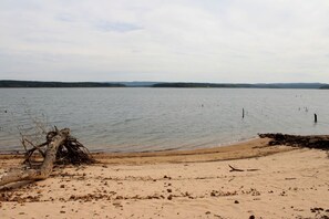 A beach with a fallen tree trunk, calm water, and distant land. - Breathtaking Wooden Cabin with Great Sights in Edgemont, Arkansas (Edgemont)