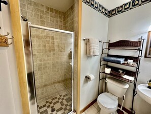 Un baño con ducha de vidrio, inodoro y estante con toallas y artículos de aseo.