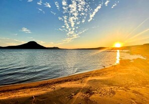 Una playa con un atardecer, agua tranquila y una montaña distante.