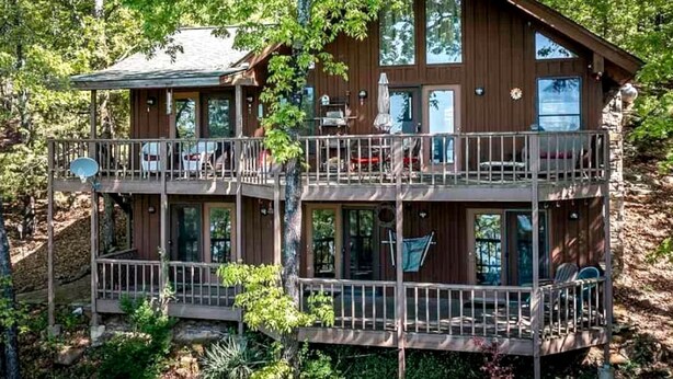 A multi-level cabin with balconies, large windows, and a natural forest setting.