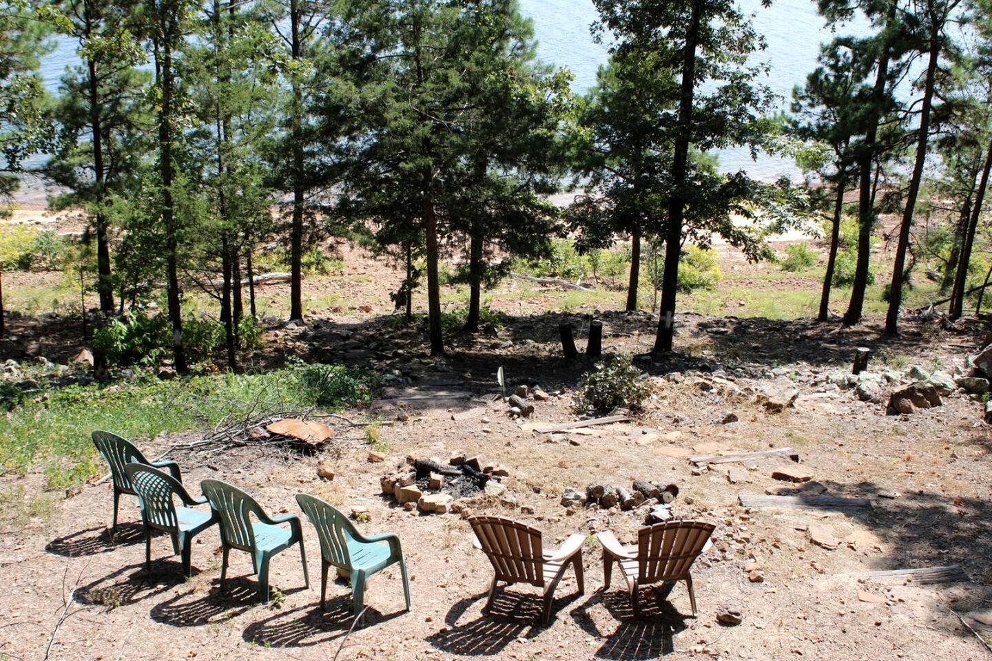 A campsite with chairs and a fire pit, surrounded by trees and a clear view of the sky.