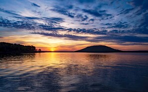 Atardecer sobre una masa de agua tranquila con una tierra firme a lo lejos.