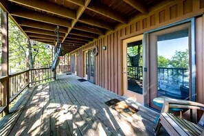 Eine überdachte Holzterrasse mit Metallgeländer, einer Tür zu einem Balkon und einer Treppe.
