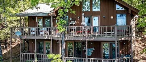 A multi-level cabin with balconies, large windows, and a natural forest setting.