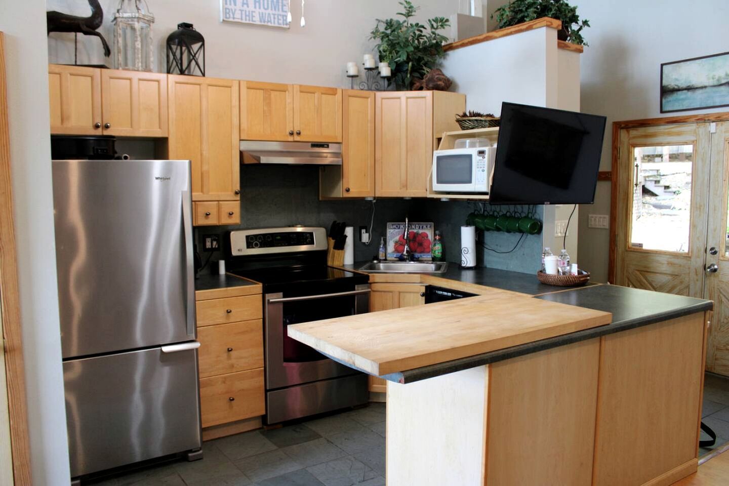 Una cucina con mobili in legno, elettrodomestici in acciaio inossidabile, un forno a microonde e un televisore a schermo piatto.