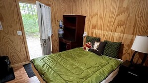 Una habitación con paneles de madera, una cama, una mesita de noche, una lámpara y un ventanal.