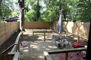 Eine Holzterrasse mit Tisch und Stühlen, einem Sonnenschirm und einem roten Gegenstand auf einem Tisch.