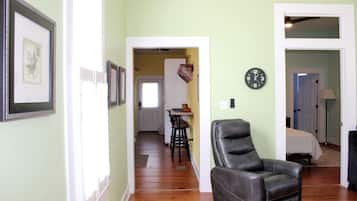 Un couloir orné de tableaux encadrés, un fauteuil en cuir, un coin repas avec une table et des chaises, et une horloge au mur.