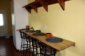 Una cocina con barra de madera, sillas negras y pared amarilla.